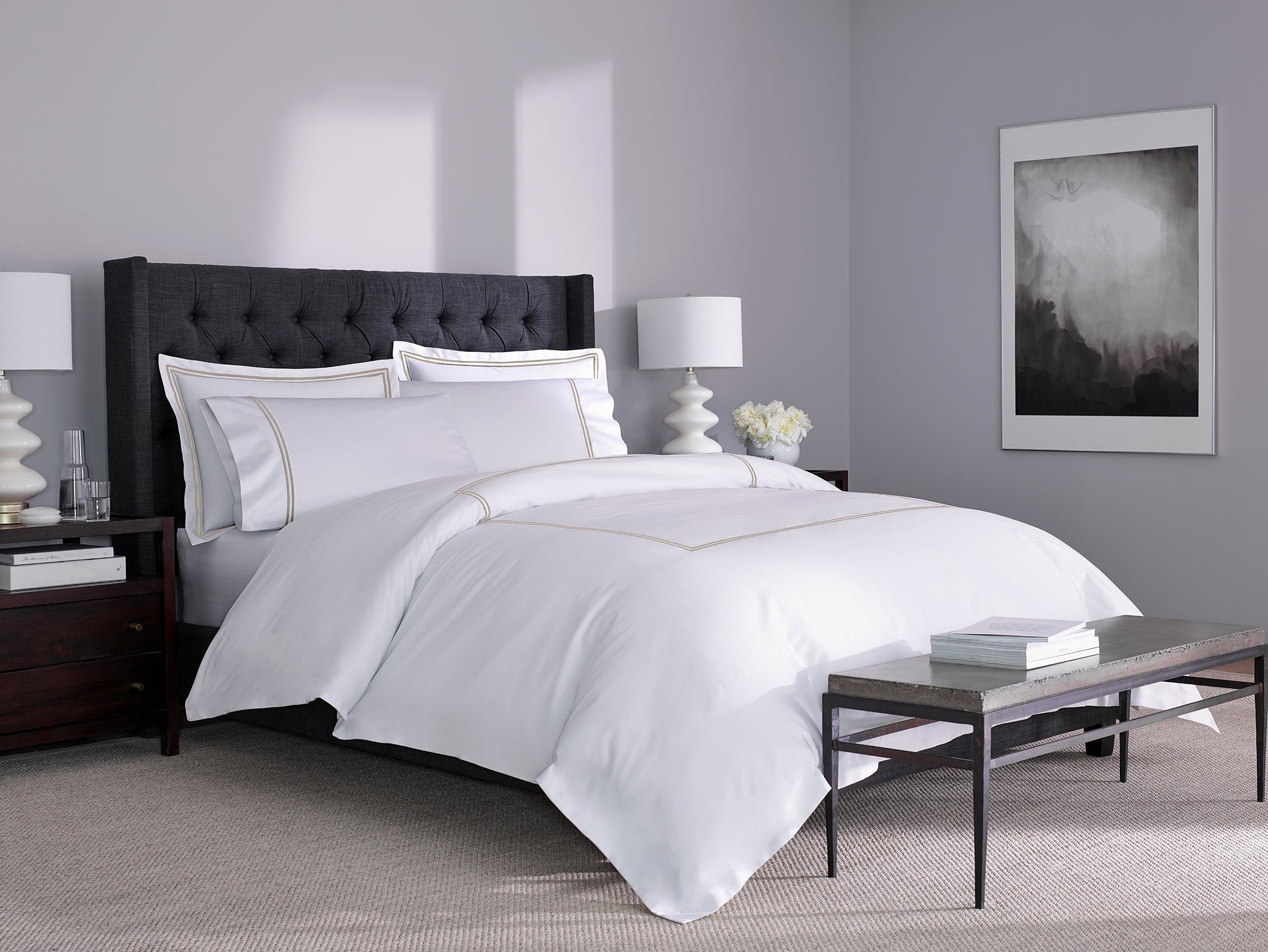 Side angle of a white cotton bed sheet with warm taupe stitching on a bed in a modern bedroom, highlighting its breathable fabric and clean finish